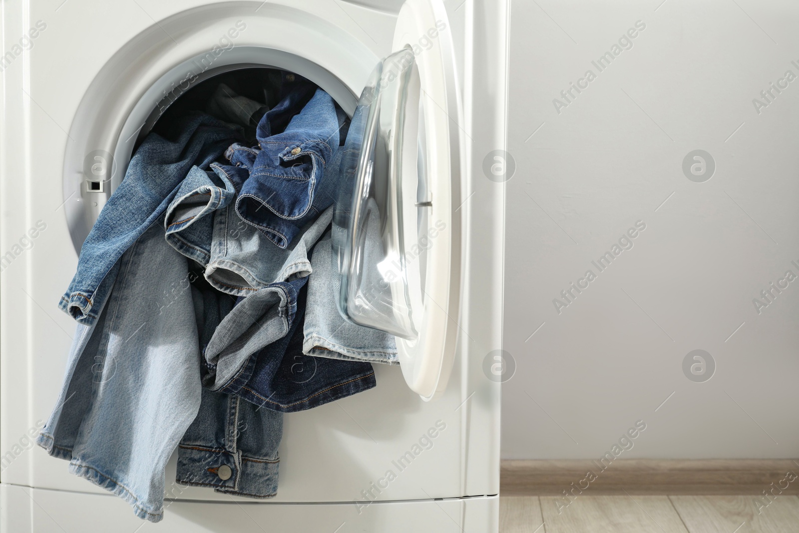 Photo of Washing machine with dirty jeans and other denim clothes indoors, space for text