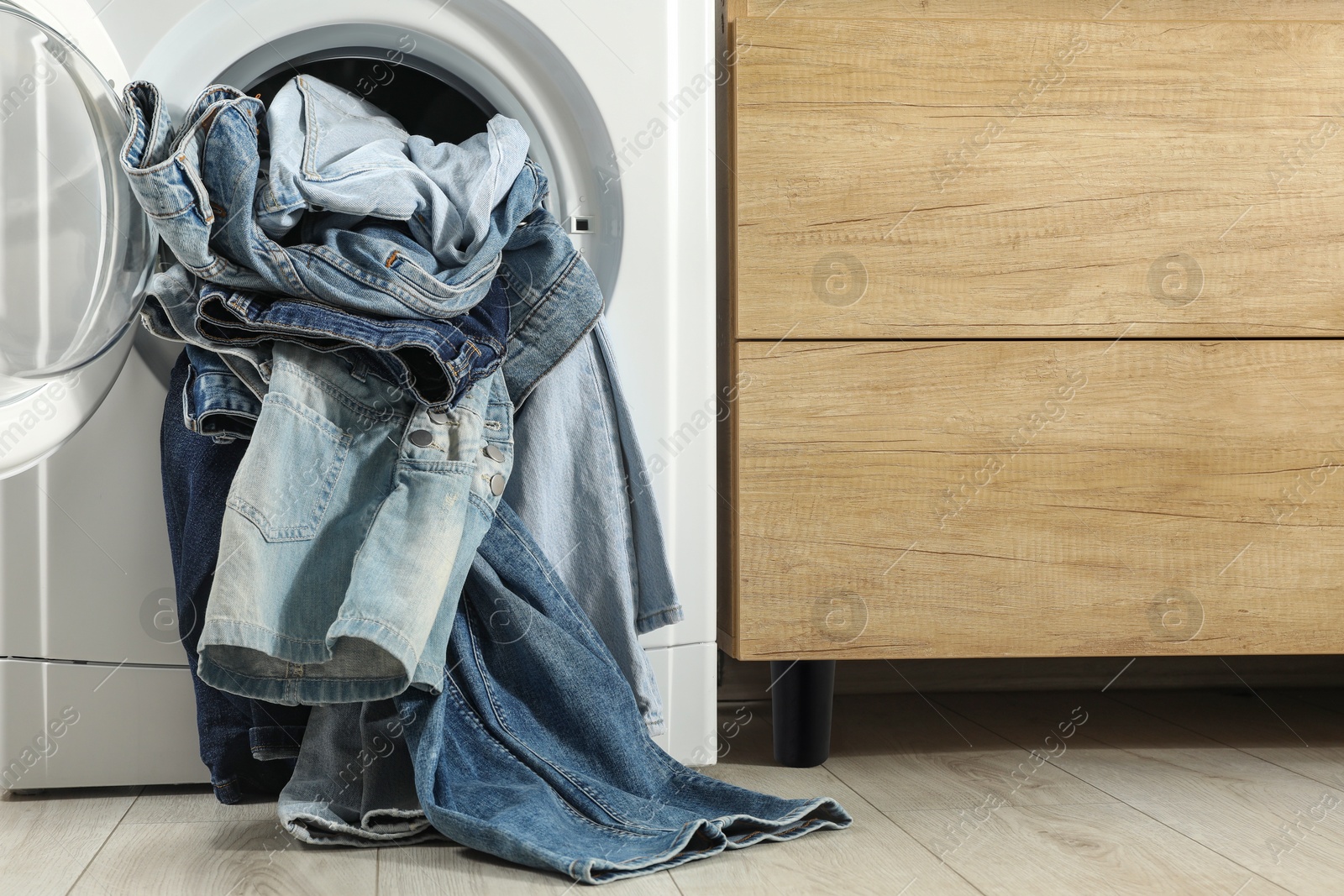 Photo of Washing machine with dirty jeans and other denim clothes indoors, space for text