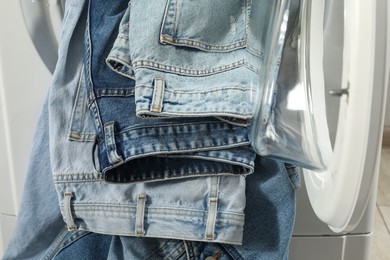 Photo of Washing machine with dirty jeans and other denim clothes indoors, closeup