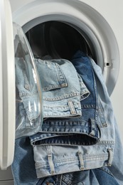 Photo of Washing machine with dirty jeans and other denim clothes indoors, closeup