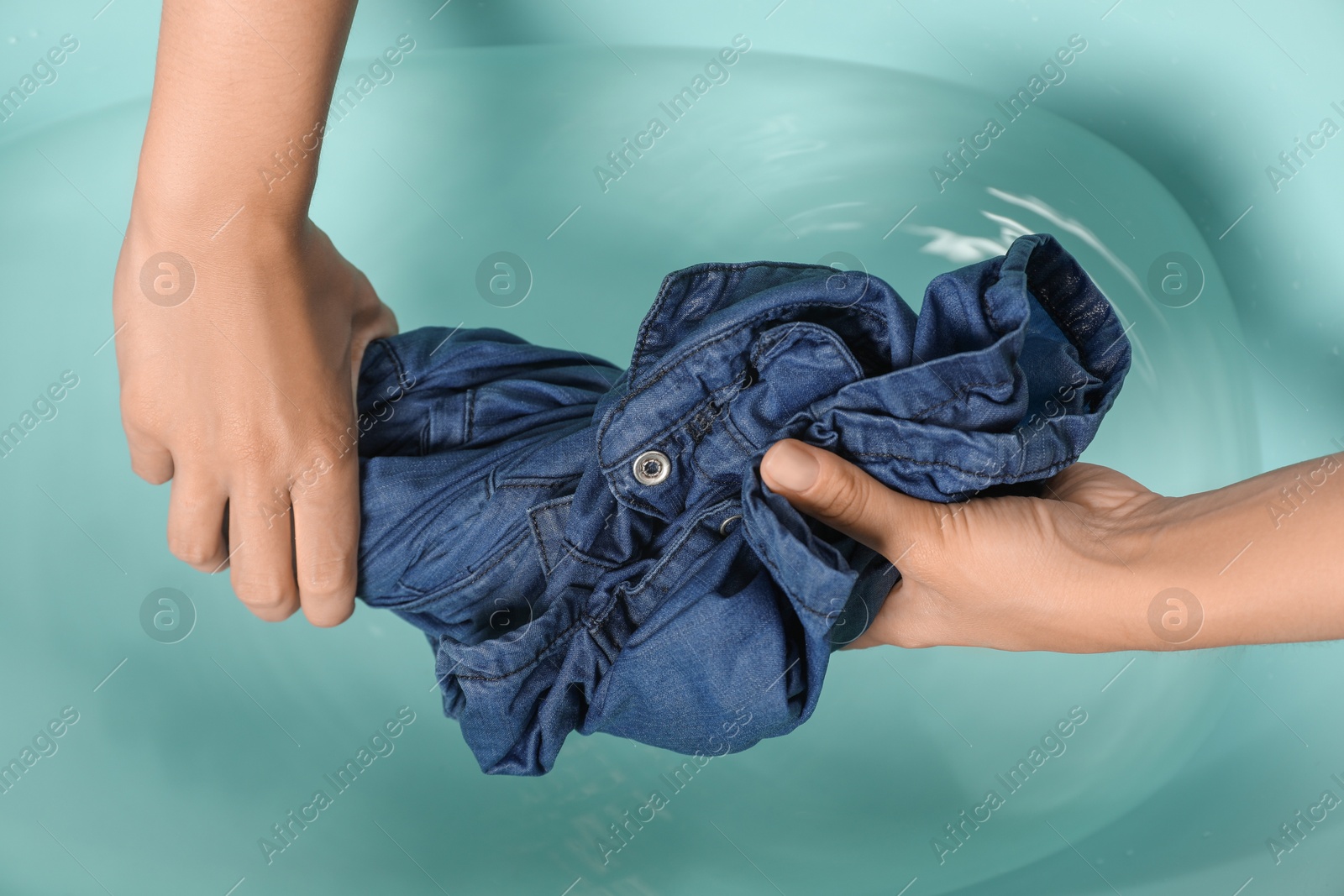 Photo of Woman washing denim clothes in basin, top view