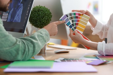 Photo of Designers with color samples working together at table in office, closeup