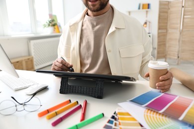 Designer with paper cup of drink using tablet at table in office, closeup