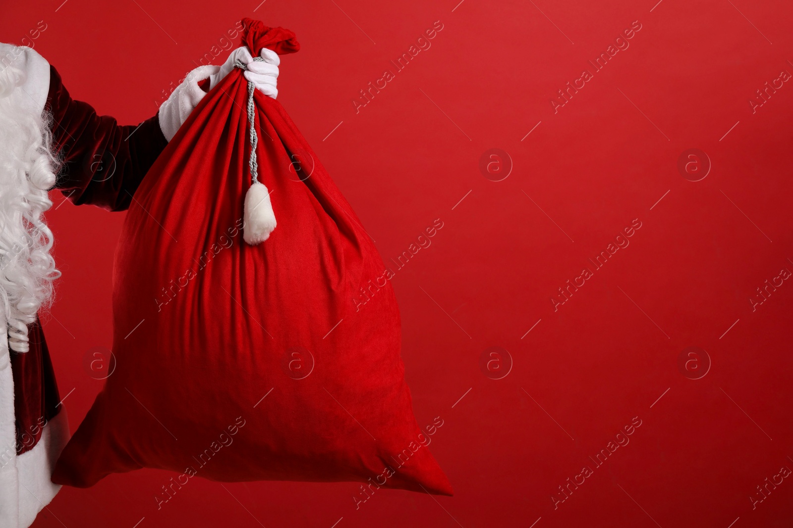 Photo of Santa Claus with bag of Christmas gifts on red background, closeup. Space for text