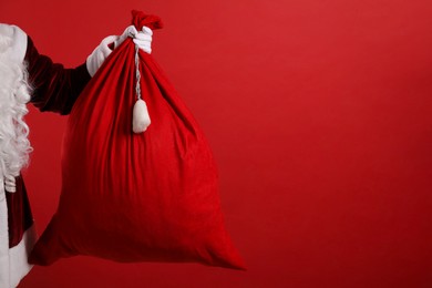 Photo of Santa Claus with bag of Christmas gifts on red background, closeup. Space for text