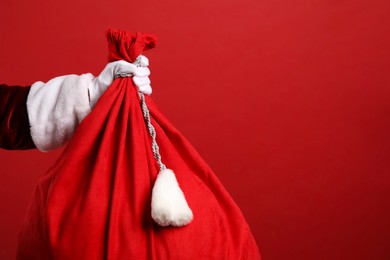 Photo of Santa Claus with bag of Christmas gifts on red background, closeup. Space for text