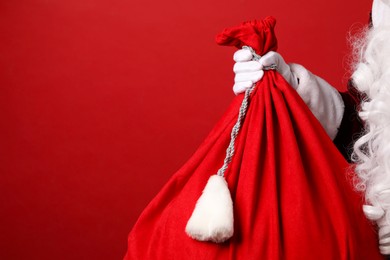 Photo of Santa Claus with bag of Christmas gifts on red background, closeup. Space for text