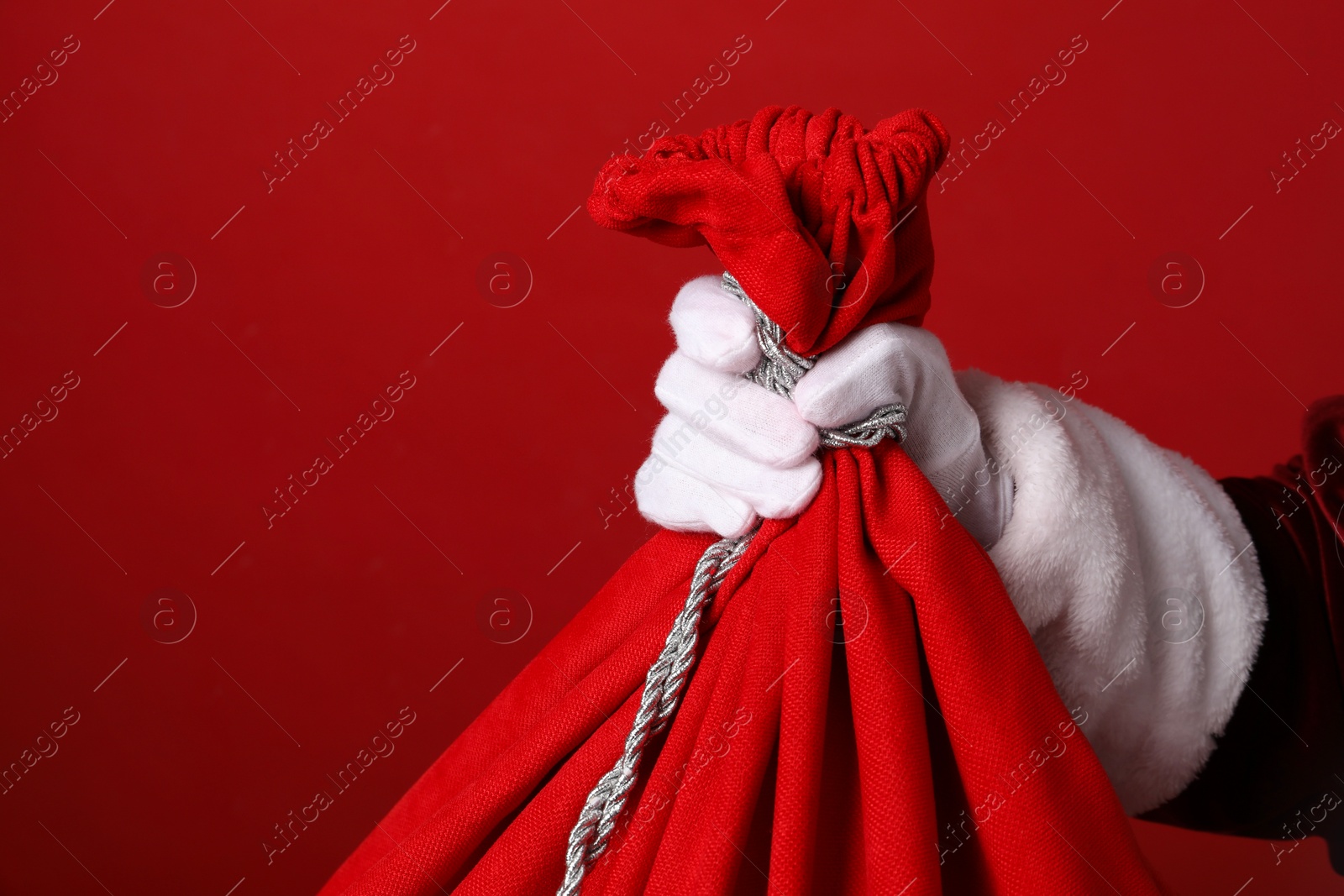 Photo of Santa Claus with bag of Christmas gifts on red background, closeup