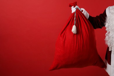 Photo of Santa Claus with bag of Christmas gifts on red background, closeup. Space for text