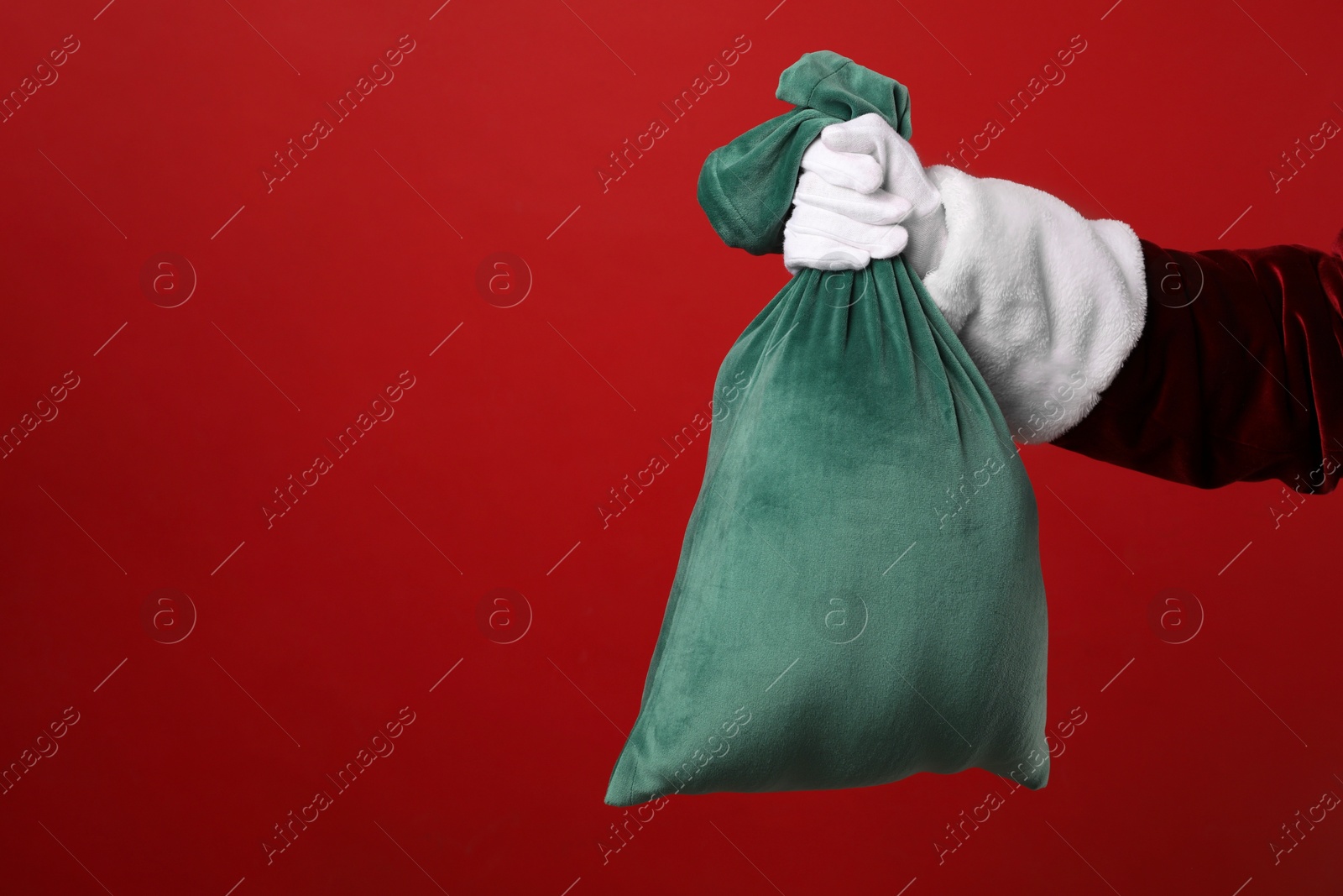 Photo of Santa Claus with green bag of Christmas gifts on red background, closeup. Space for text