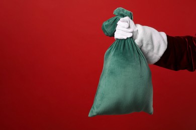 Photo of Santa Claus with green bag of Christmas gifts on red background, closeup. Space for text