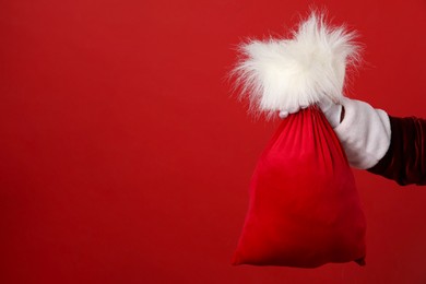 Photo of Santa Claus with bag of Christmas gifts on red background, closeup. Space for text