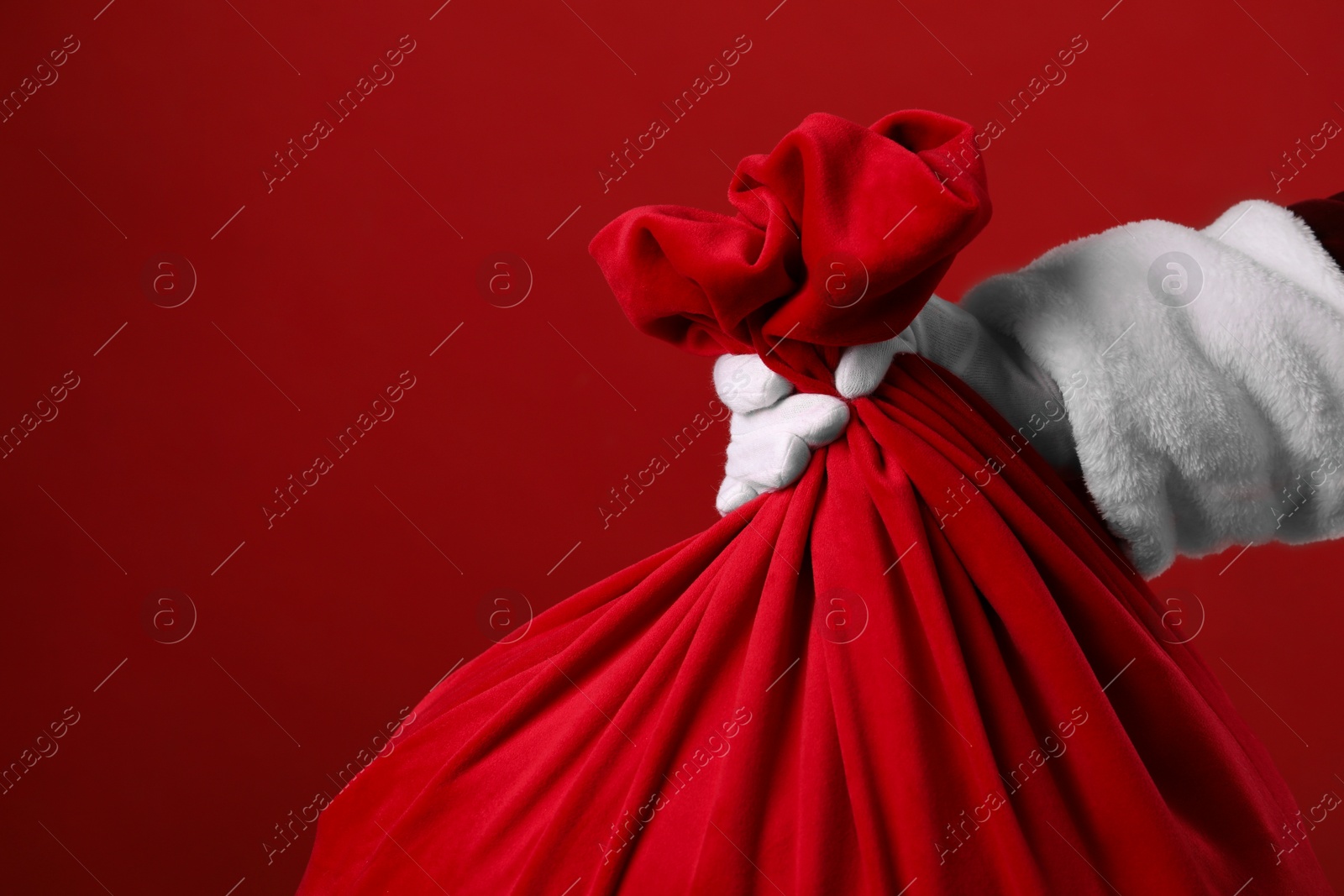 Photo of Santa Claus with bag of Christmas gifts on red background, closeup