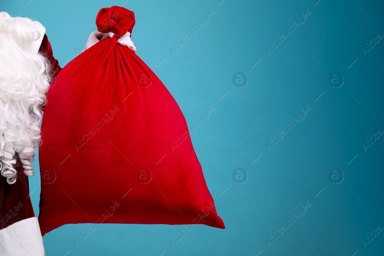 Photo of Santa Claus with red bag of Christmas gifts on light blue background, closeup. Space for text