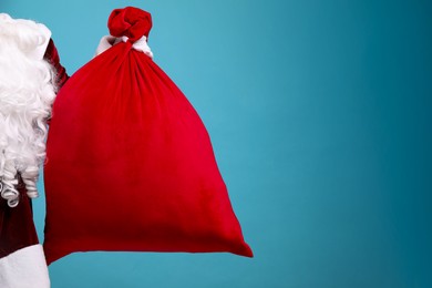 Photo of Santa Claus with red bag of Christmas gifts on light blue background, closeup. Space for text