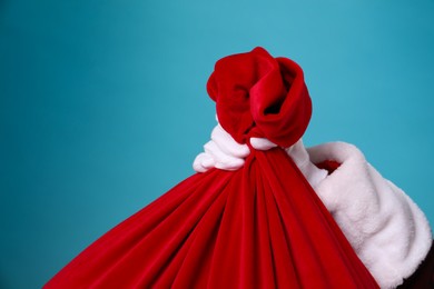 Photo of Santa Claus with red bag of Christmas gifts on light blue background, closeup