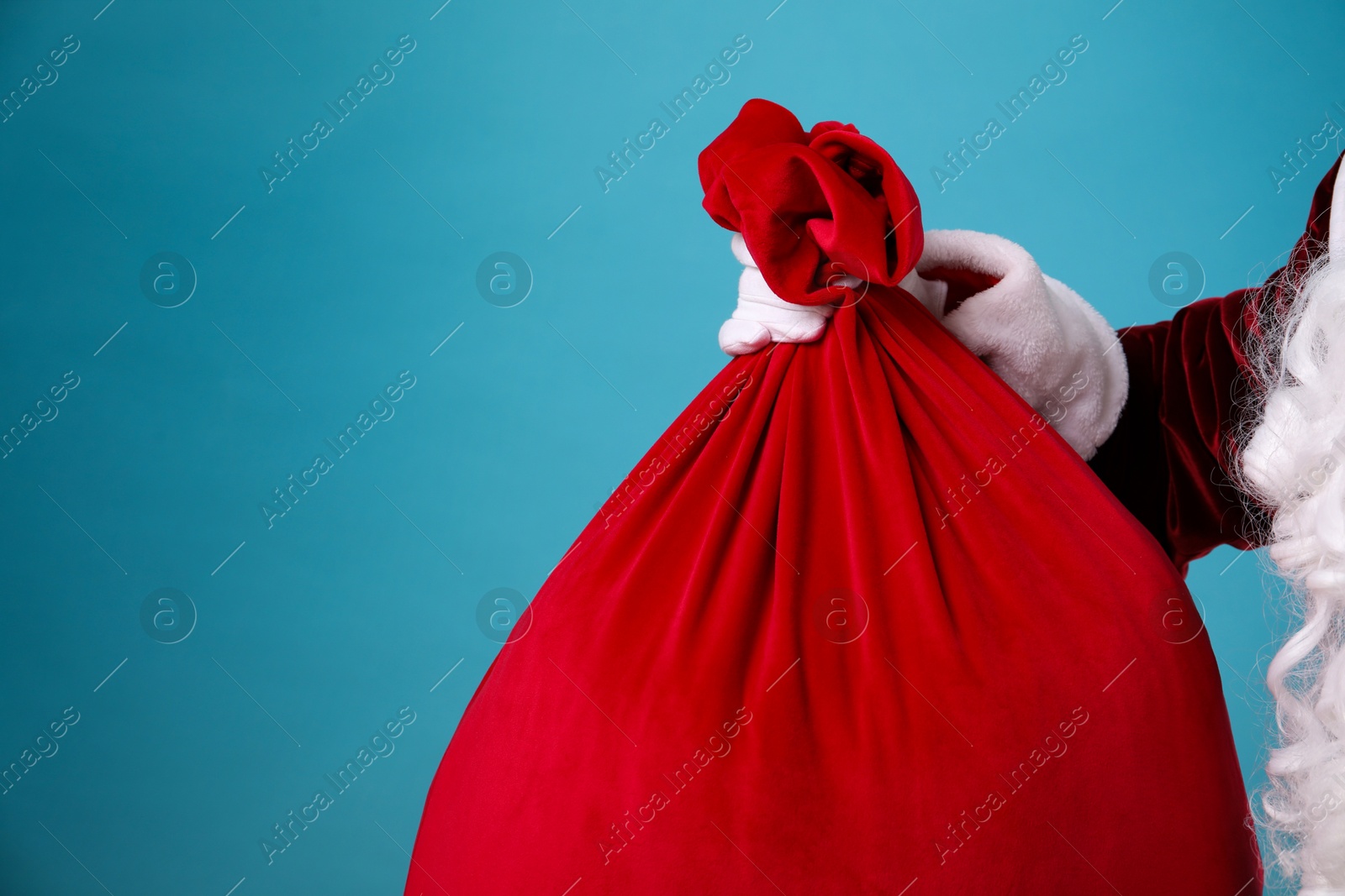 Photo of Santa Claus with red bag of Christmas gifts on light blue background, closeup