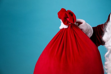 Photo of Santa Claus with red bag of Christmas gifts on light blue background, closeup