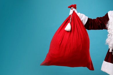 Photo of Santa Claus with red bag of Christmas gifts on light blue background, closeup. Space for text