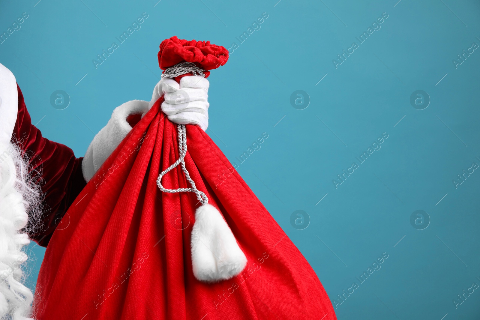 Photo of Santa Claus with red bag of Christmas gifts on light blue background, closeup