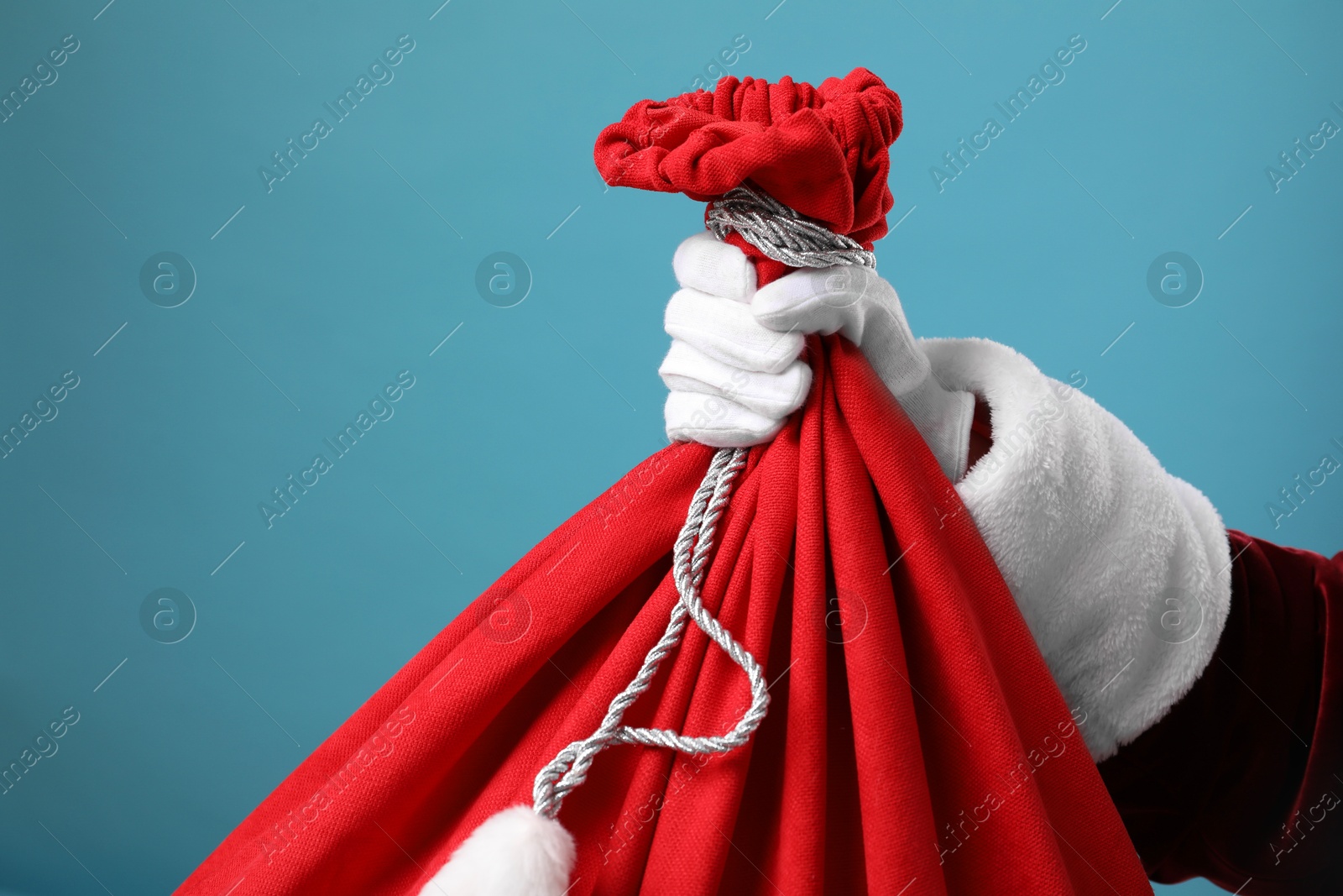 Photo of Santa Claus with red bag of Christmas gifts on light blue background, closeup