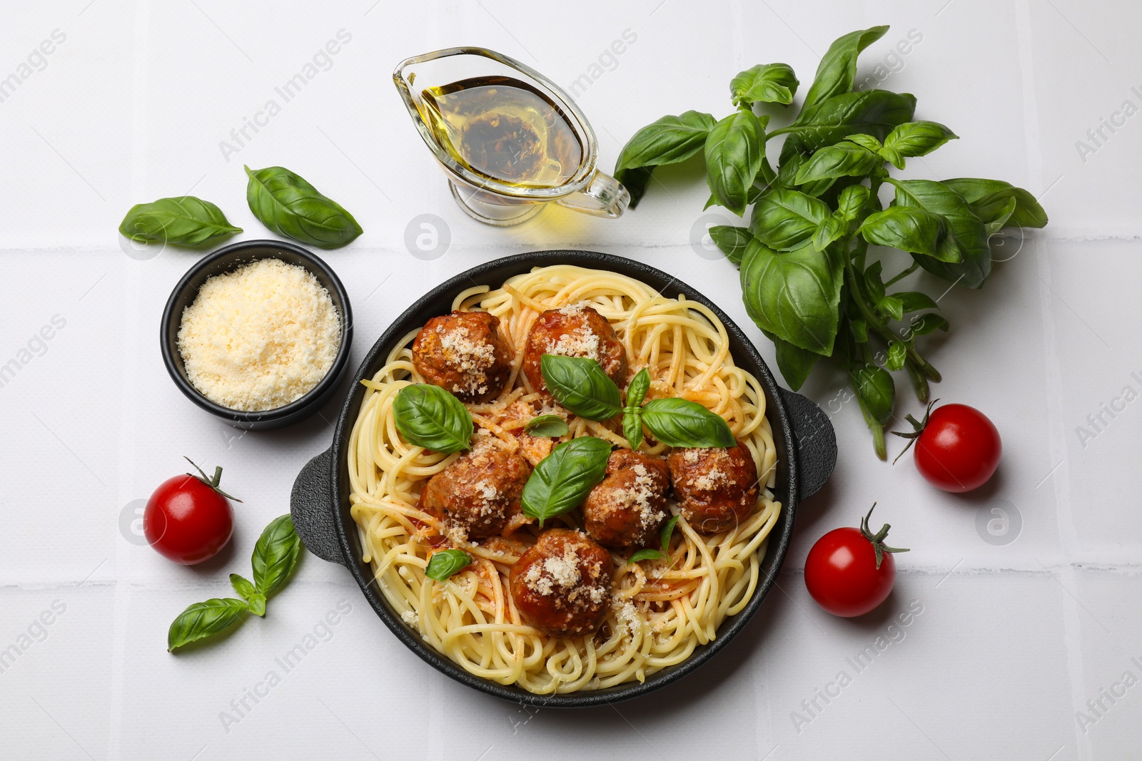 Photo of Delicious pasta with meatballs and ingredients on white tiled table, flat lay