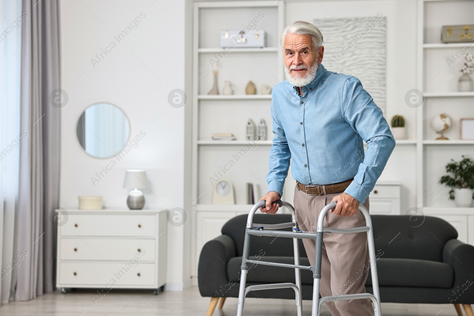 Photo of Senior man using walking frame at home. Space for text