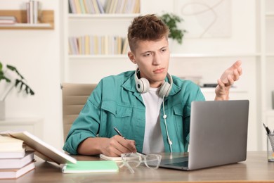 Photo of Student with headphones studying at table indoors