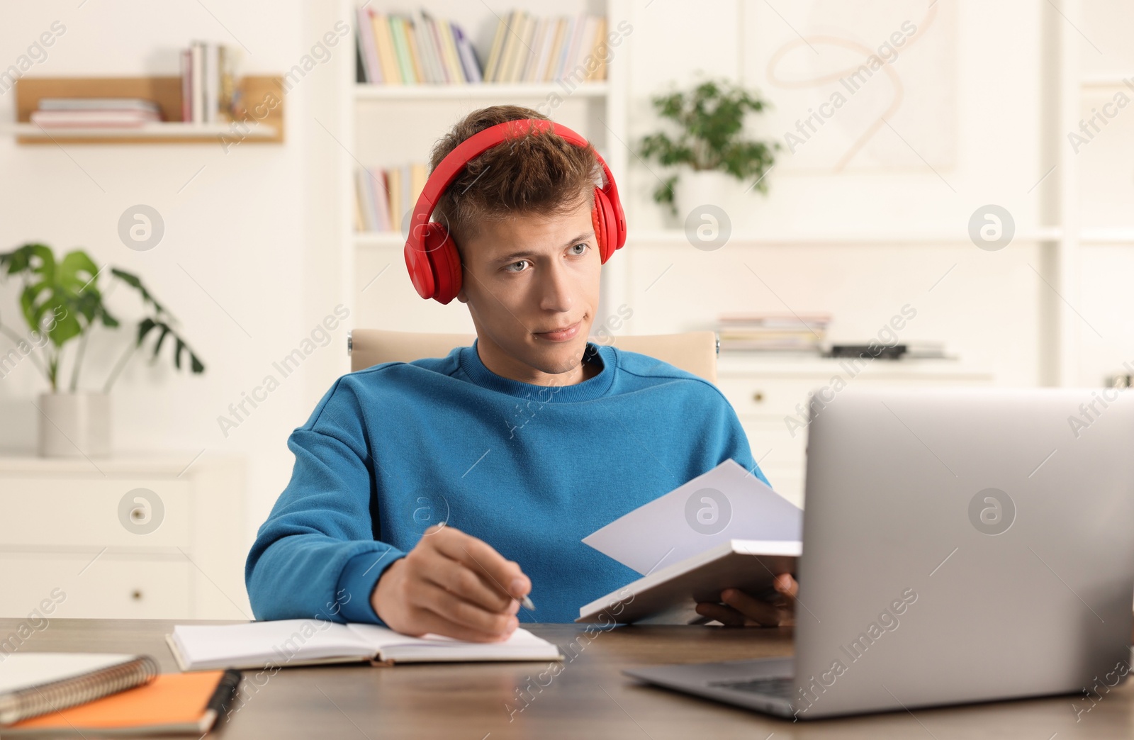 Photo of Student in headphones taking notes while studying at table indoors