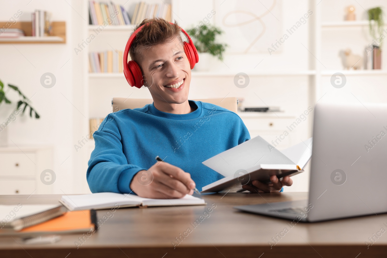 Photo of Student in headphones taking notes while studying at table indoors