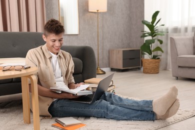 Photo of Student with book and laptop studying on floor at home