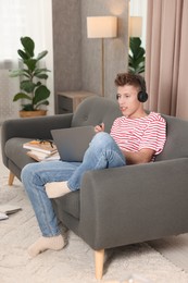 Photo of Student in headphones studying with laptop on sofa at home