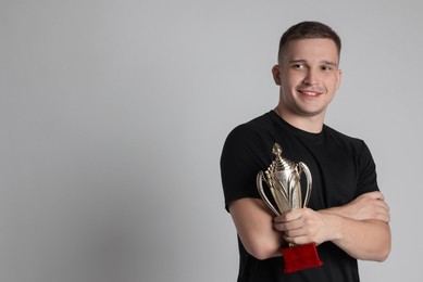 Photo of Happy winner with golden trophy cup on light grey background, space for text