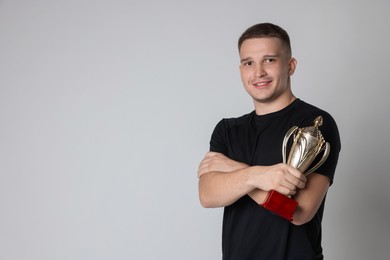 Photo of Happy winner with golden trophy cup on light grey background, space for text