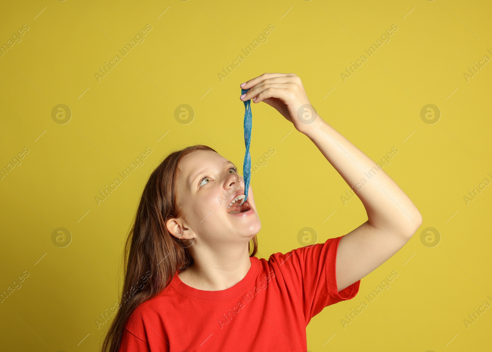 Photo of Teenage girl eating tasty gummy candy on yellow background