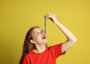 Photo of Teenage girl eating tasty gummy candy on yellow background