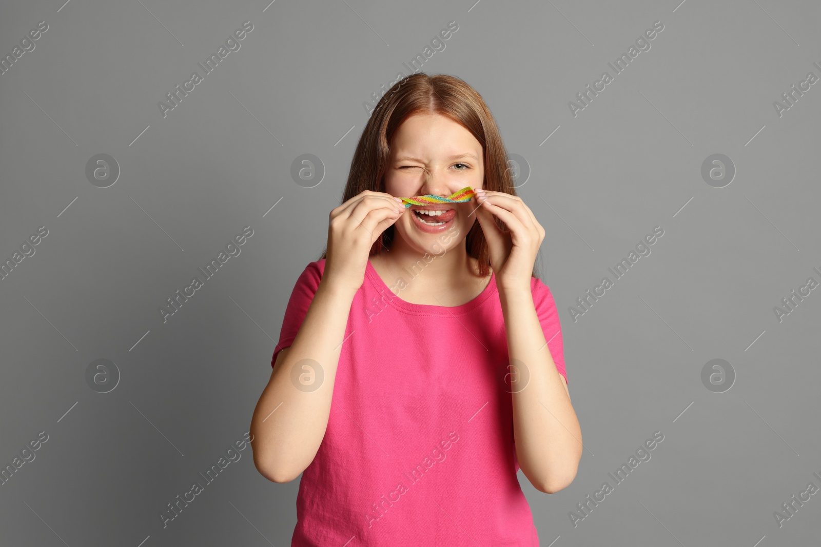 Photo of Happy teenage girl with tasty rainbow sour belt on grey background