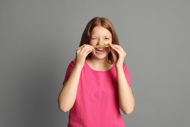 Photo of Happy teenage girl with tasty rainbow sour belt on grey background