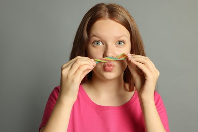 Photo of Funny teenage girl with tasty rainbow sour belt on grey background