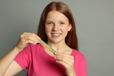 Photo of Happy teenage girl with tasty rainbow sour belt on grey background