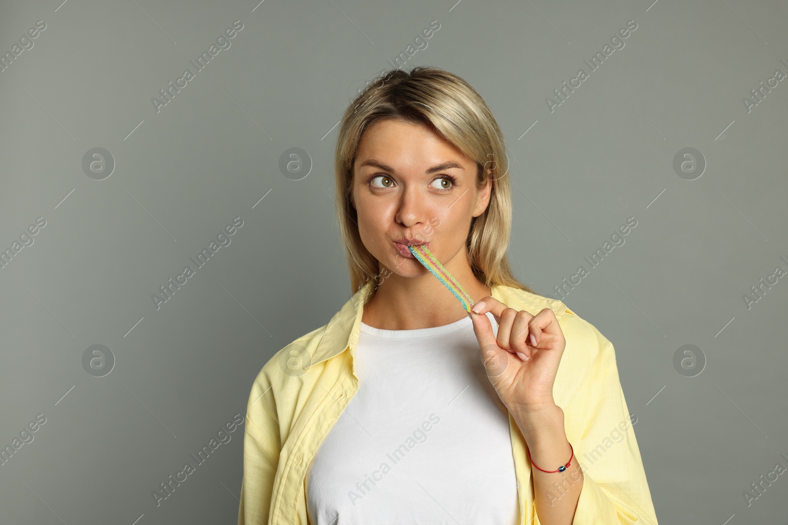 Photo of Young woman eating tasty rainbow sour belt on grey background