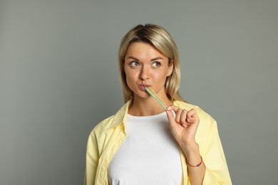 Photo of Young woman eating tasty rainbow sour belt on grey background