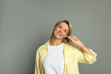 Photo of Young woman eating tasty rainbow sour belt on grey background