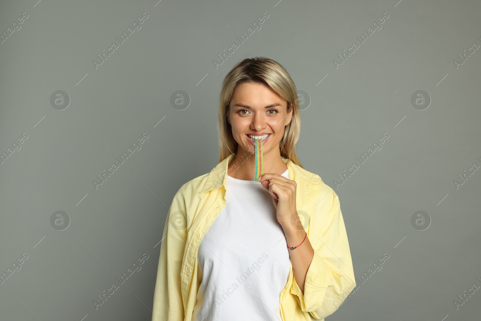 Photo of Young woman eating tasty rainbow sour belt on grey background