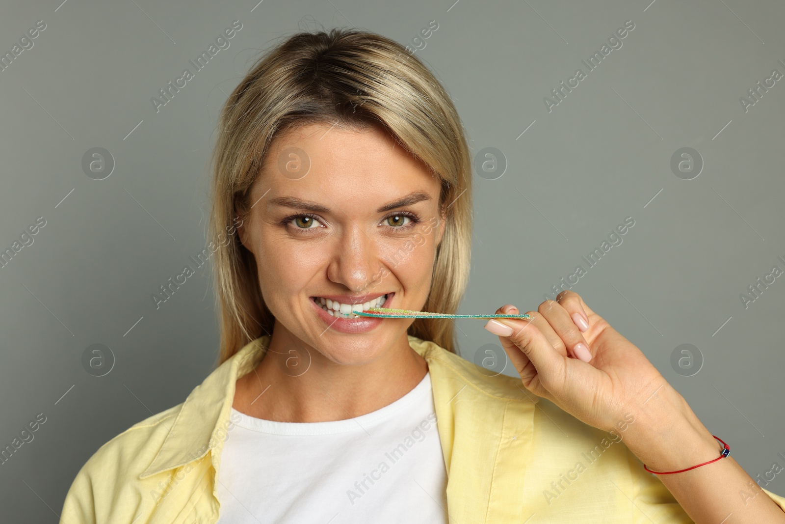 Photo of Young woman eating tasty rainbow sour belt on grey background