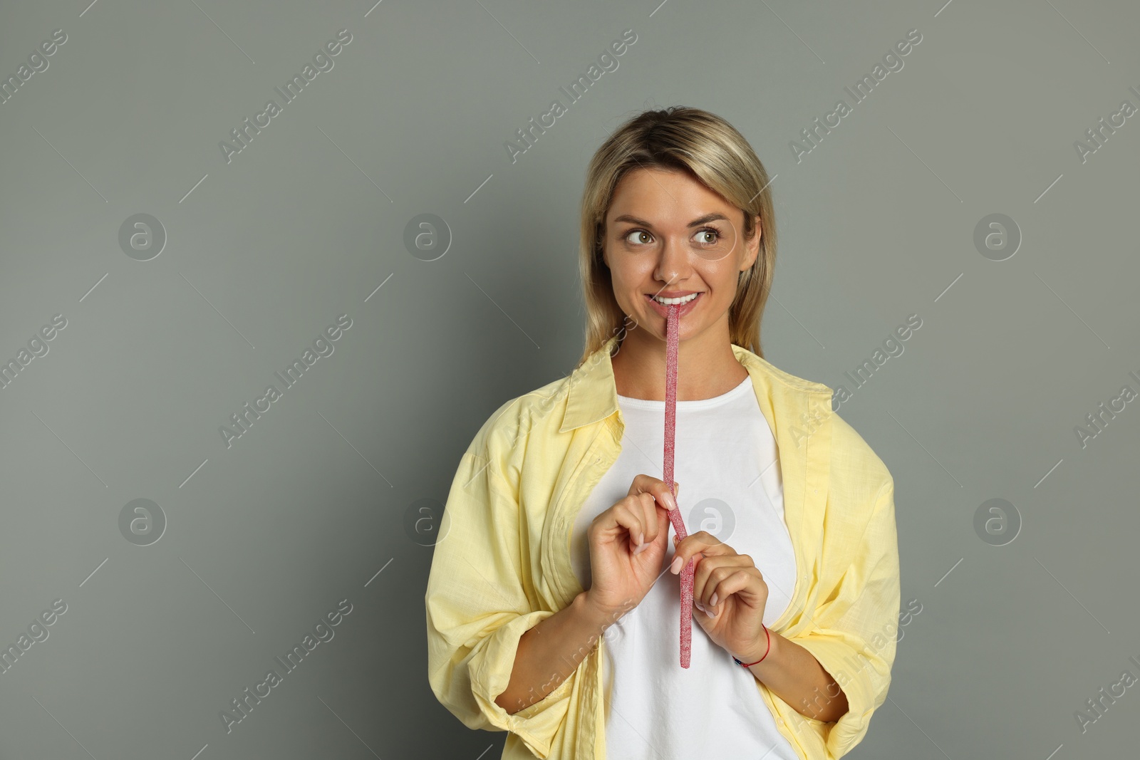 Photo of Young woman eating tasty gummy candy on grey background