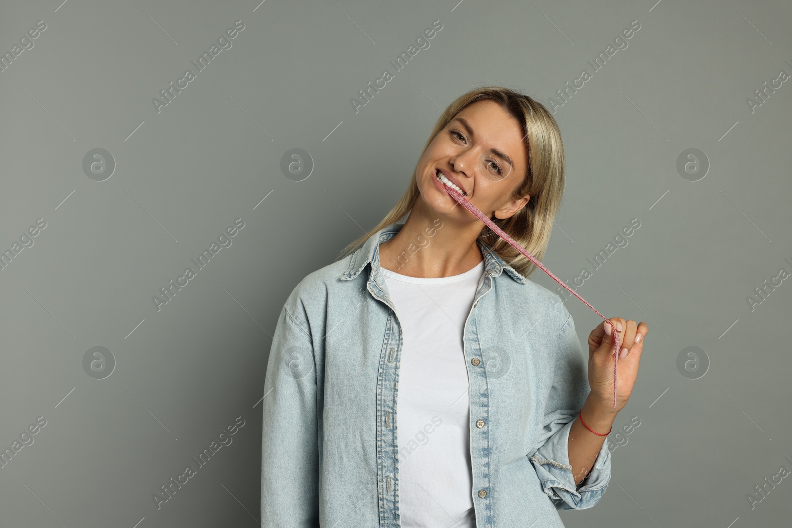 Photo of Young woman eating tasty gummy candy on grey background