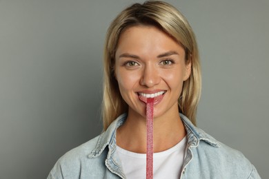 Photo of Young woman eating tasty gummy candy on grey background