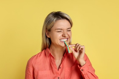 Photo of Young woman eating tasty rainbow sour belt on yellow background