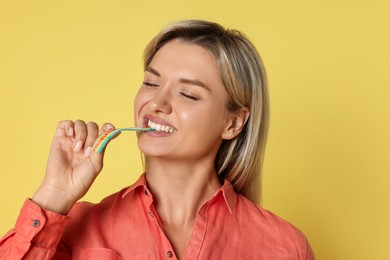 Photo of Young woman eating tasty rainbow sour belt on yellow background